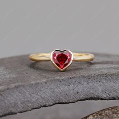 a heart shaped ring with a red stone in the middle on top of a rock