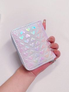 a woman's hand holding a pink and white wallet with hearts on the front