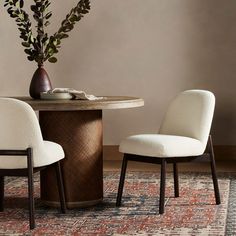 two chairs sitting at a round table with a vase on top of it next to a rug