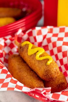 two hotdogs with mustard on them in a red and white checkered basket