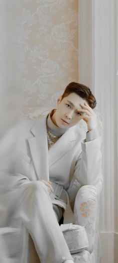 a man sitting on top of a white chair in front of a window with his hands to his face