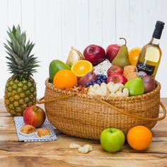 a basket filled with lots of fruit next to a pineapple and bottle of wine