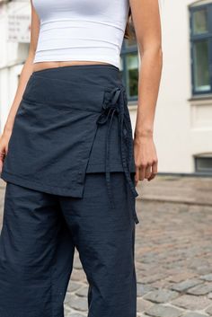 a woman in white top and blue pants standing on brick road with her hands behind her back