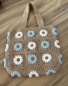 a crocheted bag with blue and white daisies on it sitting on a wooden floor