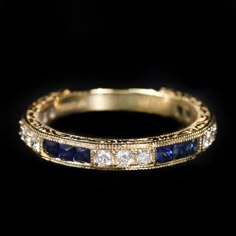 a yellow gold ring with blue sapphires and diamonds on the side, against a black background