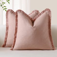 two pink pillows sitting on top of a white couch next to a potted plant