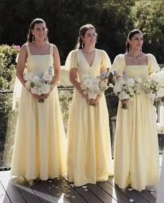 three bridesmaids in yellow dresses standing on a wooden deck with white bouquets