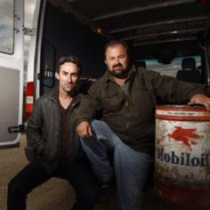 two men sitting next to each other in front of a van