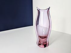 a pink glass vase sitting on top of a white table next to a blue wall