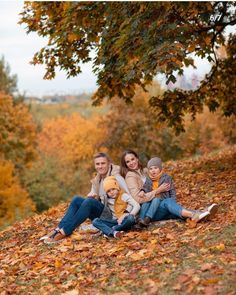 a family is sitting on the ground with autumn leaves