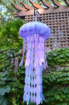 a purple and blue jellyfish hanging from a metal hook on a vine covered fence