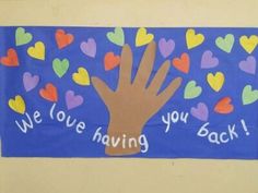 a bulletin board with a hand and hearts on it that says we love having you back