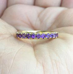 a woman's hand holding a yellow gold ring with purple stones