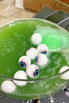 some balls with eyes are in a green bowl filled with water and soapy bubbles