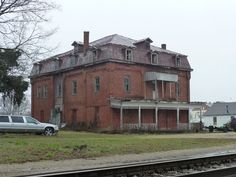 an old red brick building sitting on the side of a road next to a train track