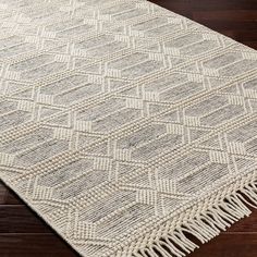 a white rug with fringes on top of a wooden floor next to a window