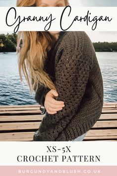 a woman wearing a brown cardigan standing next to the water with her arms around her neck