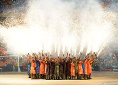 a group of people standing next to each other on top of a field holding up their hands