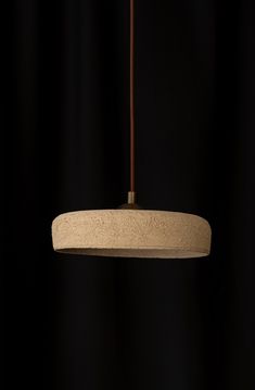 a light fixture hanging from a ceiling in front of a black curtained background with a wooden stick sticking out of it