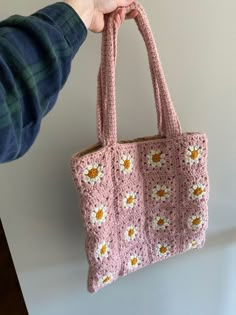 a hand holding a pink crocheted bag with yellow flowers on the front and bottom