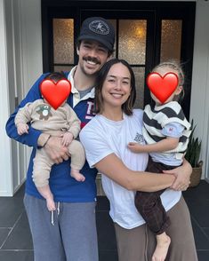 a man and woman holding two babys in front of a door with hearts on them