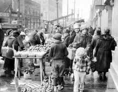 an old black and white photo of people shopping in the street with produce for sale