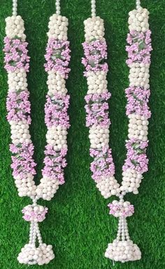 three white and pink necklaces with flowers hanging from them on green grass in the sun