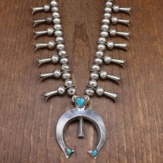 Very nice vintage sterling silver and turquoise squash blossom necklace. The naja is stamped "R" with an arrow-like symbol mark. The work appears to be Navajo. The necklace is a 25.5" single strand of 12mm sterling beads. Each side of the necklace has seven all-silver 1 1/2"-long blossoms. The sand-cast naja measures 3" tall by 2 5/16" wide. It has a hidden bail and is removable. The turquoise at the top of the naja is 10mm long. The stones at the tips are 6.5mm. The necklace shows normal wear b Like Symbol, Turquoise Squash Blossom, Squash Blossom Necklace, Squash Blossom, Tucson, Vintage Sterling Silver, Stone Color, Necklace Etsy, Beaded Necklace