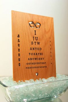 a wooden sign with glasses on it sitting in a glass bowl filled with seaglass