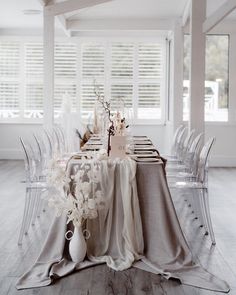 the table is set with clear chairs and white flowers in vases on each side