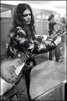 a man playing an electric guitar in a room with other people standing around and looking at it