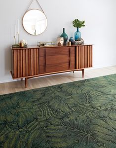 a living room with a green rug, mirror and wooden furniture on the sideboard