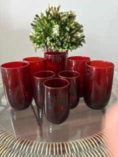 red glass cups sitting on top of a table next to a potted plant