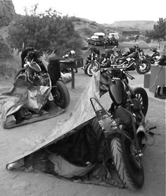 several motorcycles are parked on the side of a dirt road with tarp covering them