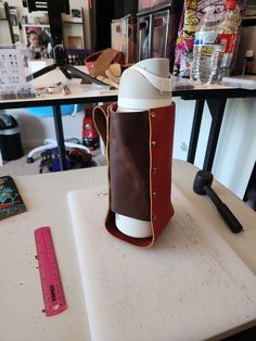 a leather cup holder sitting on top of a white table next to a ruler and other items