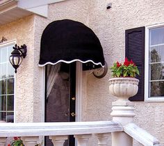 a white house with a black awning over it's door and flower box