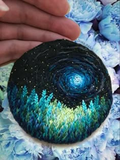 a hand is holding a painted rock with blue flowers in the background and a sky filled with stars