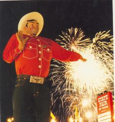 a man in a red shirt and cowboy hat standing next to fireworks