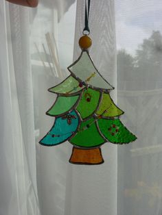 a stained glass christmas tree ornament hanging from a window sill in front of a white curtain