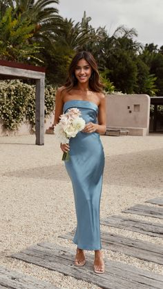 a woman in a strapless blue dress holding a white bouquet and posing for the camera