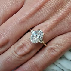 a woman's hand with a diamond ring on top of her finger and the other hand holding an engagement ring