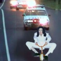 a woman riding a bike down a street next to a car and another vehicle on the road