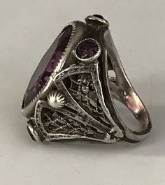 "This lovely filigreed and ornate ring has an oval shaped faceted amethyst purple color glass stone at its center. It is flanked on either side of to and bottom with small round bezel set purple glass stones. The sides have lattice shaped cut outs and the band is smooth. The face of this ring is about 3/4\" long and about 1/2\" across. It is a size 3 1/4 and is marked Sterling. Please note there are some overall signs of wear, especially to the stones, four of five of which, including the center Oval Amethyst Jewelry Collectible, Antique Oval Amethyst Ring, Antique Oval Purple Amethyst Ring, Oval Amethyst Collectible Ring, Antique Oval Purple Jewelry, Antique Purple Oval Jewelry, Heirloom Oval Purple Jewelry, Antique Oval Filigree Ring Gift, Vintage Amethyst Oval Cabochon Ring