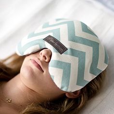 a woman laying on top of a white bed wearing a blue and white chevron sleep mask