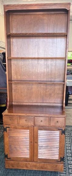 an old wooden bookcase with shutters on the front and bottom doors, sitting on carpeted flooring