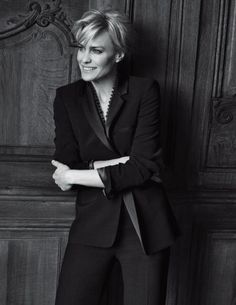 a black and white photo of a woman in a suit leaning against a wooden wall