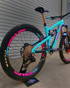 a blue and pink mountain bike parked in front of a garage door with graffiti on it