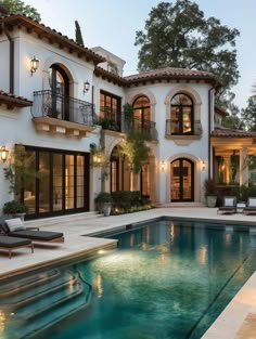 an outdoor swimming pool in front of a large white house with lots of windows and doors