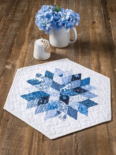 a blue and white quilted table topper next to a vase with hydrangeas