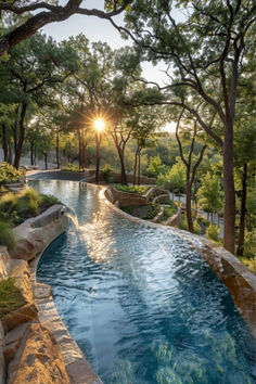 an outdoor swimming pool surrounded by trees and bushes with the sun setting in the background